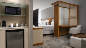 Een hotelkamer met een bed, een bureau met een computer, een magnetron, een koelkast en een glazen plank met een koffiezetapparaat.