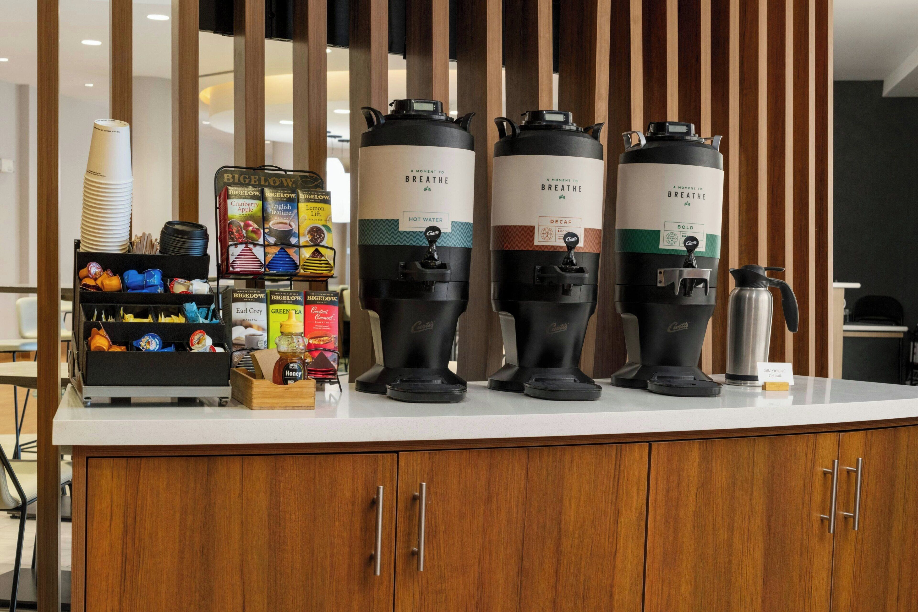 A coffee station with two coffee makers, a coffee pot, and a variety of coffee cups and containers.