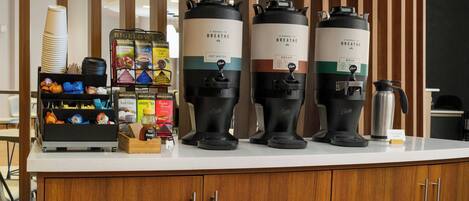 A coffee station with two coffee makers, a coffee pot, and a variety of coffee cups and containers.