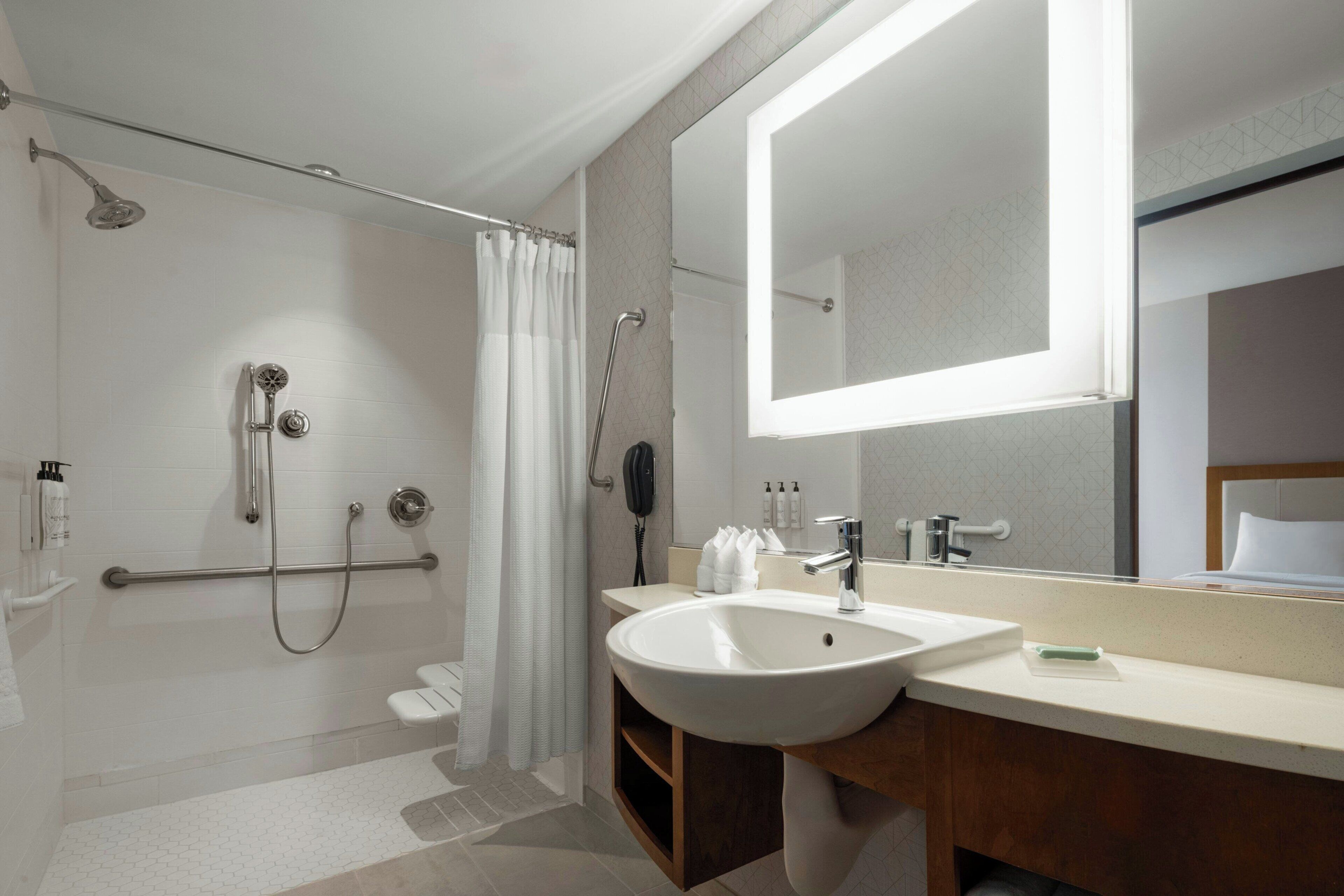 Une salle de bain moderne dotée d’une douche à l’italienne, d’un grand miroir et d’un lavabo avec un meuble-vasque en bois.