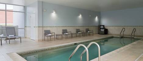 An indoor swimming pool with tiled flooring, a few lounge chairs, and a wall with a patterned border.