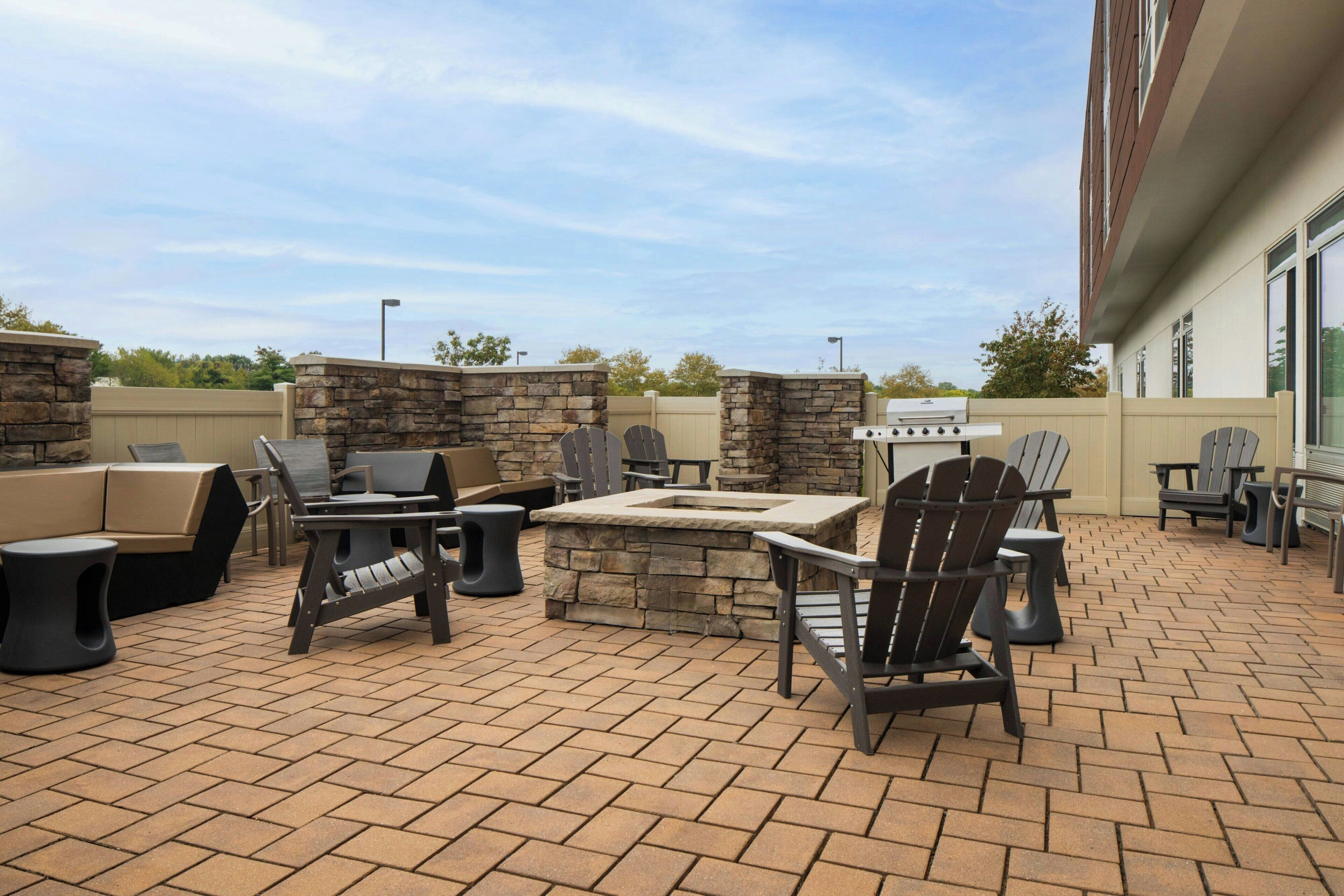 Un patio al aire libre con suelo de ladrillo, paredes de piedra y mobiliario exterior que incluye sillas, una mesa y una parrilla.