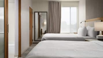 A hotel room with two beds, a large window with curtains, a mirror, and a wooden headboard.