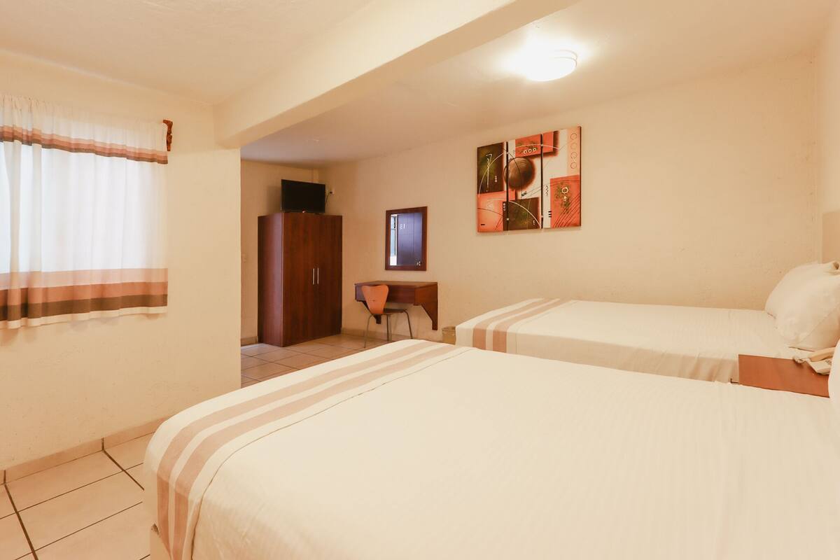 Habitación de hotel con dos camas, un escritorio, un televisor y una puerta que da a un baño.