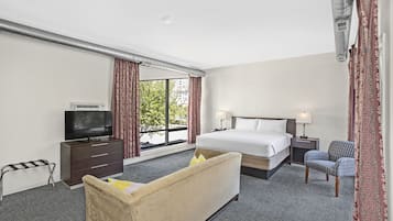Una habitación de hotel con cama, televisión, escritorio, silla y ventana con cortinas.