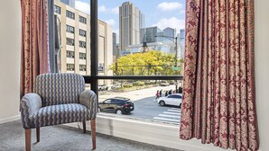Una habitación con un ventanal grande, un sillón estampado y vistas a un paisaje urbano con edificios y una calle.