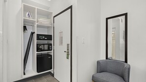 Una habitación con un armario blanco, un sofá gris y un espejo en la pared.