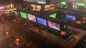 A bar area with multiple screens displaying various content, a large screen with 'BUYING IN' text, and a 'COLD DRINK' sign. - Canad Inns Destination Centre Garden City (Winnipeg)
