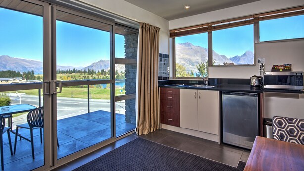 Cocina moderna con vistas a montañas, zona de comedor con mesa y sillas, y puerta corrediza de vidrio que da a un balcón.