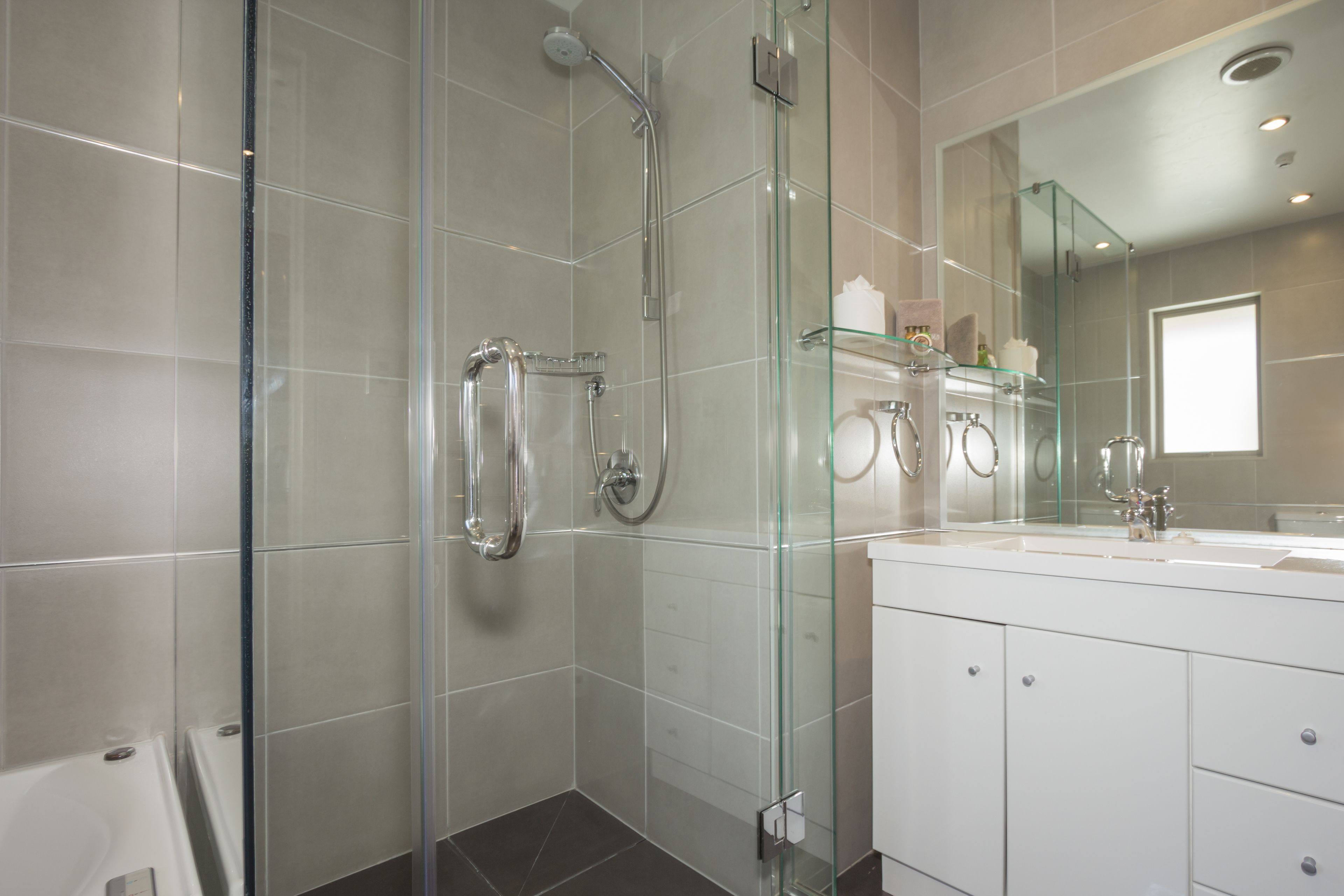 Une salle de bain moderne avec une douche à parois de verre, un meuble-lavabo blanc doté d’un grand miroir et une baignoire.