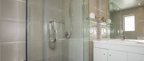 Une salle de bain moderne avec une douche à parois de verre, un meuble-lavabo blanc doté d’un grand miroir et une baignoire.