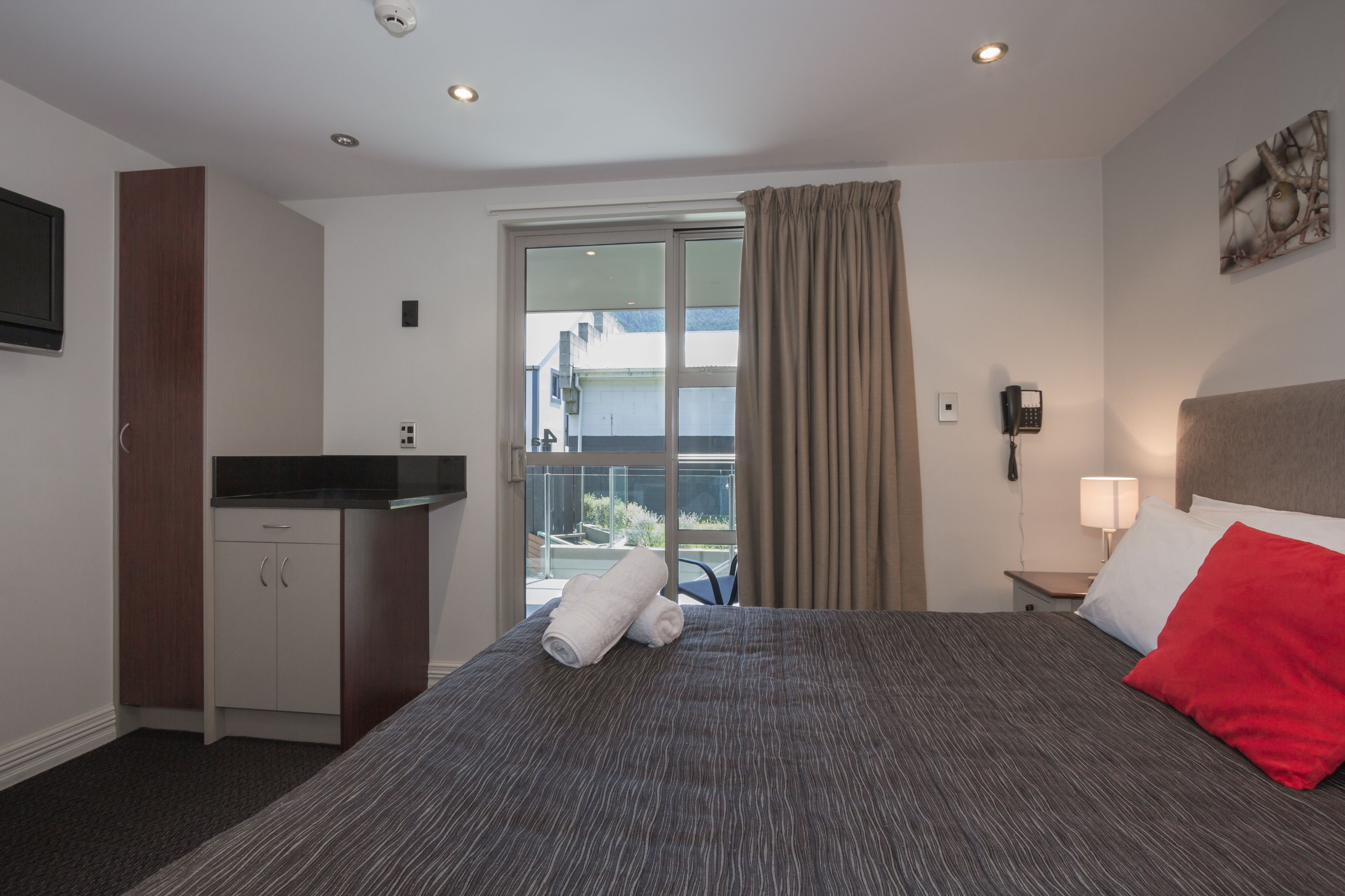 A hotel room with a bed, a desk, a telephone, and a window with curtains.