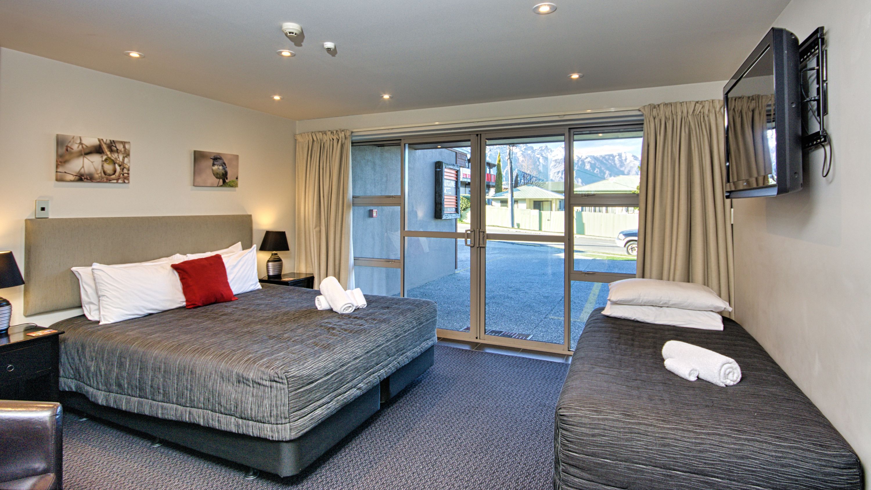 Habitación de hotel con una cama grande, una cama más pequeña, un televisor de pantalla plana y vistas al exterior.
