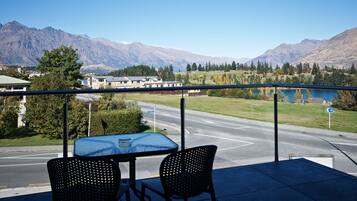 A balcony with a table and chairs overlooking a road, mountains, and a lake.