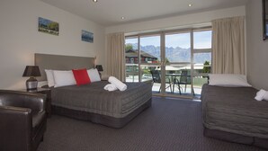 Habitación de hotel con una cama grande, una cama más pequeña, un sofá y un balcón con vista a la montaña.