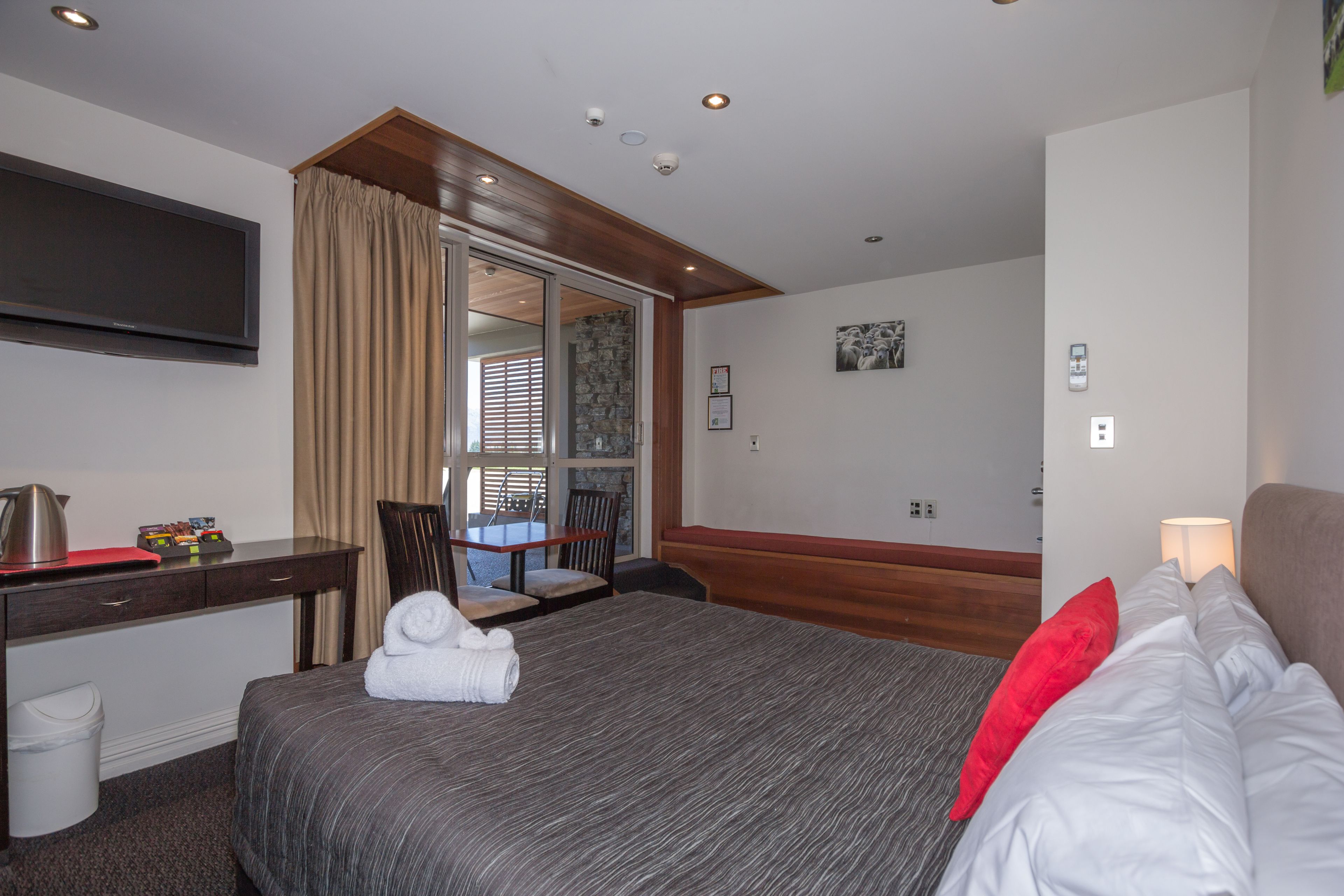 Una habitación de hotel con cama, escritorio, televisión y ventana con cortinas.