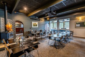 Un grand espace dédié à la salle à manger, avec plusieurs tables et chaises, un mur en briques et une grande fenêtre qui laisse entrer la lumière naturelle.