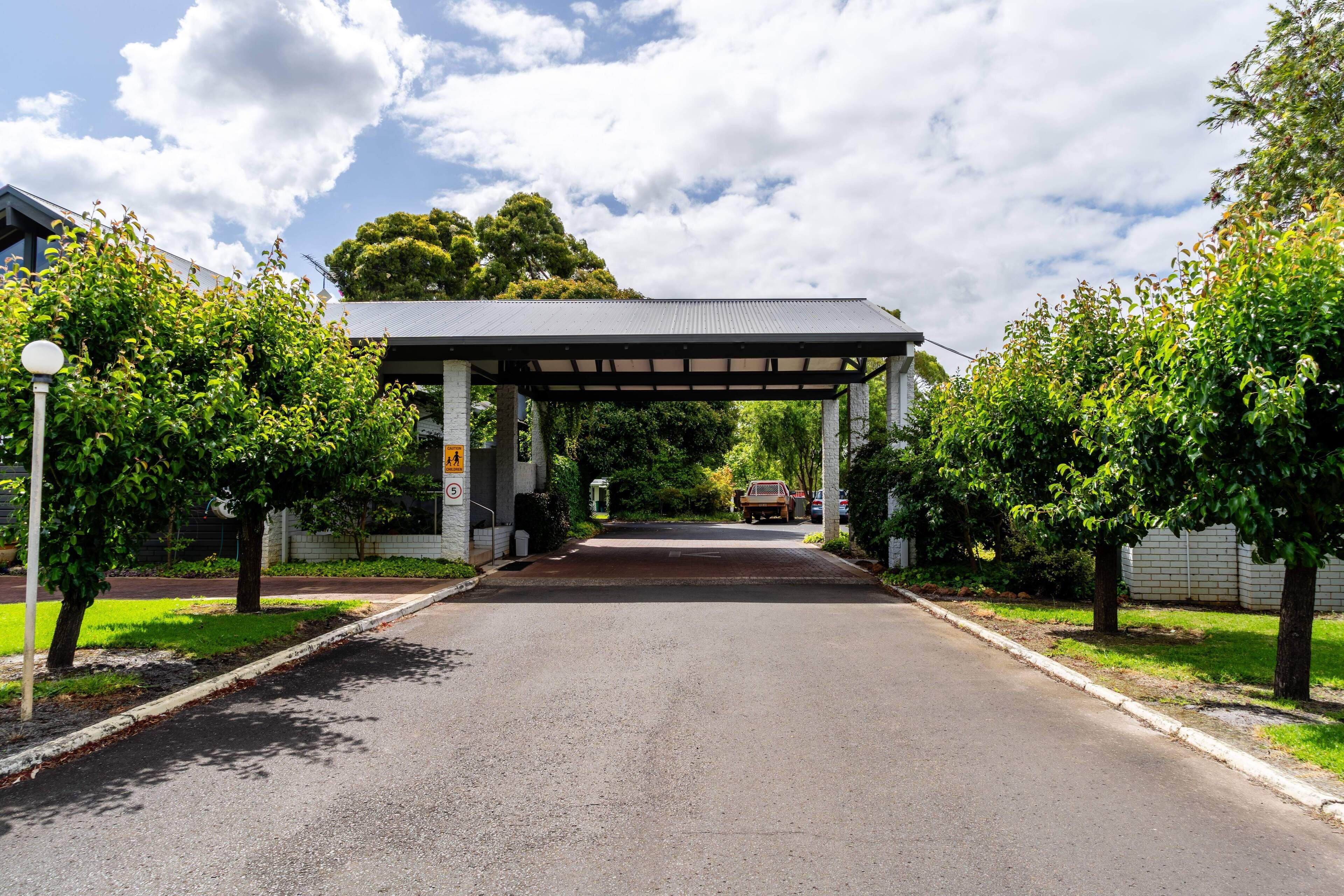 A covered walkway leading to a building with a tiled roof, surrounded by trees and a clear sky.
