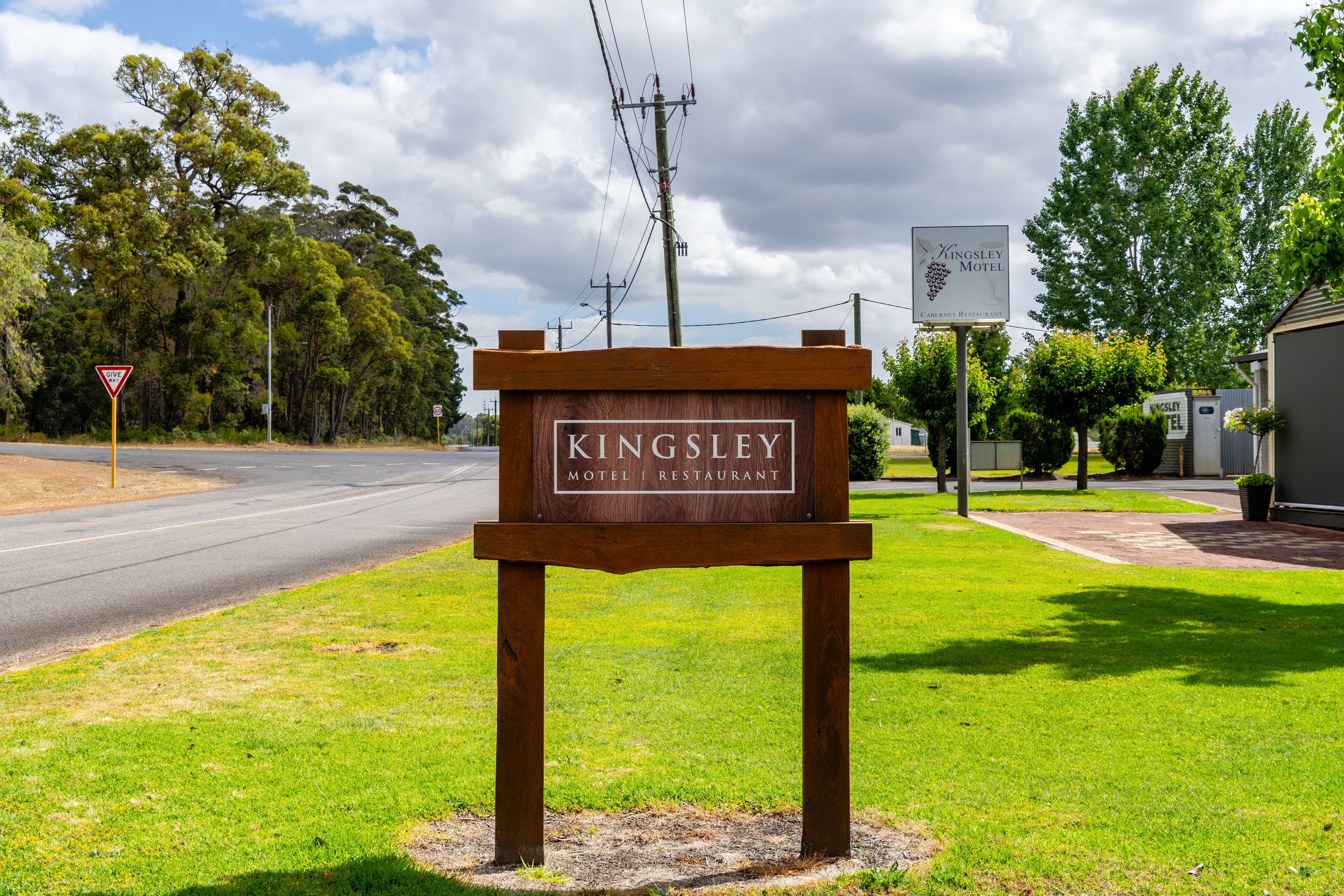 Un letrero de madera anuncia el Motel y Restaurante Kingsley, con una carretera y árboles al fondo.