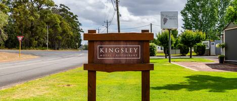 Un letrero de madera anuncia el Motel y Restaurante Kingsley, con una carretera y árboles al fondo.