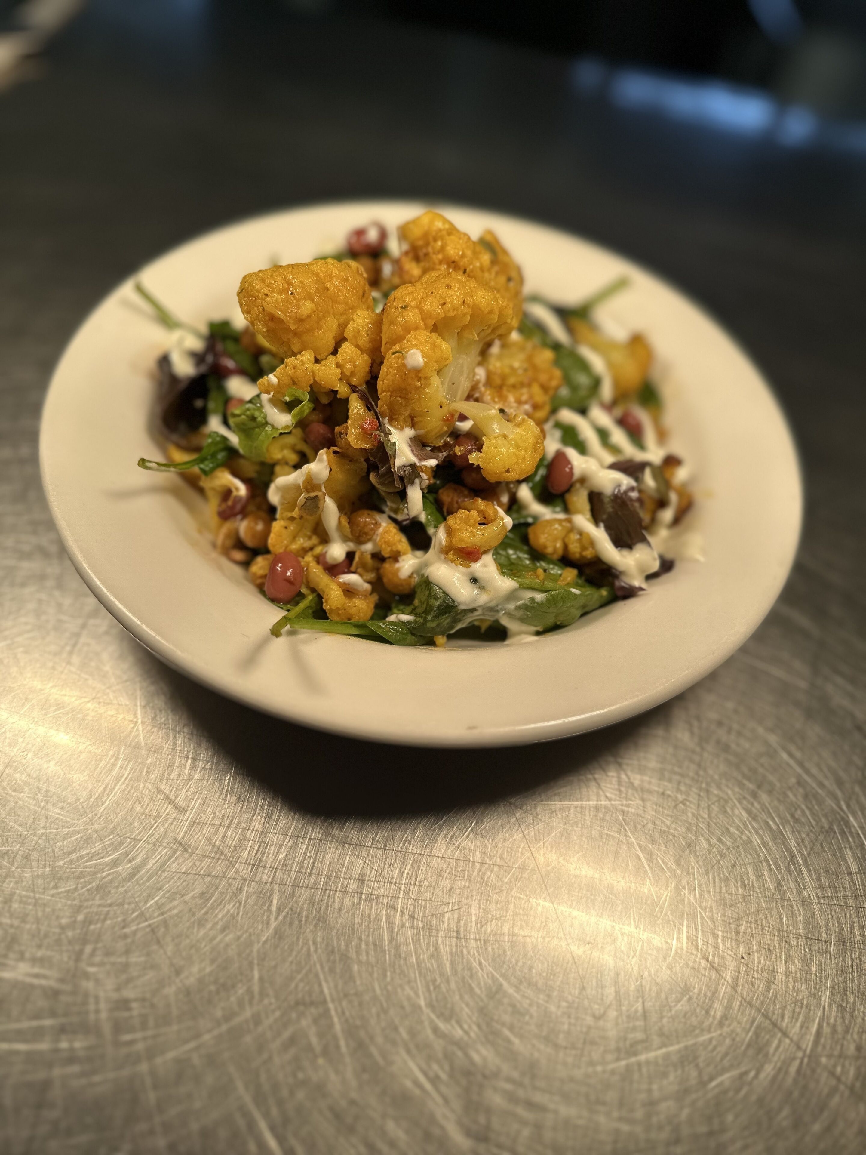 A plate of food with cauliflower, chickpeas, and greens, served on a white plate.