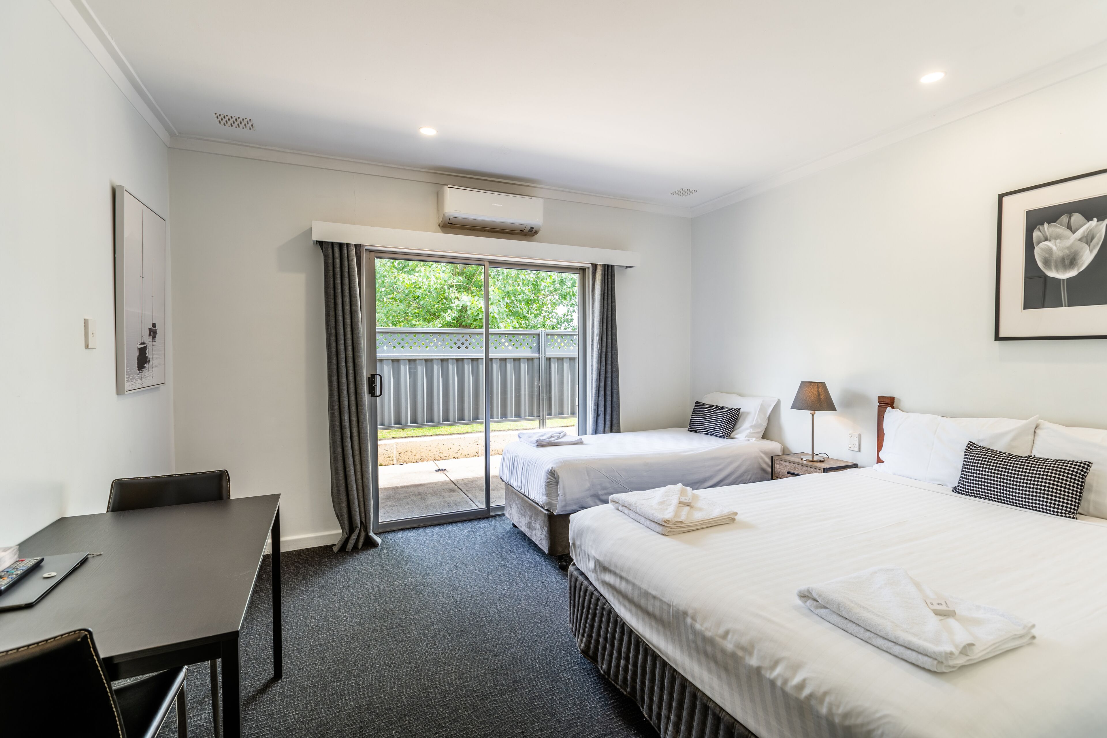 Ein Hotelzimmer mit Bett, Schreibtisch und Stuhl. Ein Fenster mit Vorhängen bietet Blick auf Grünfläche.