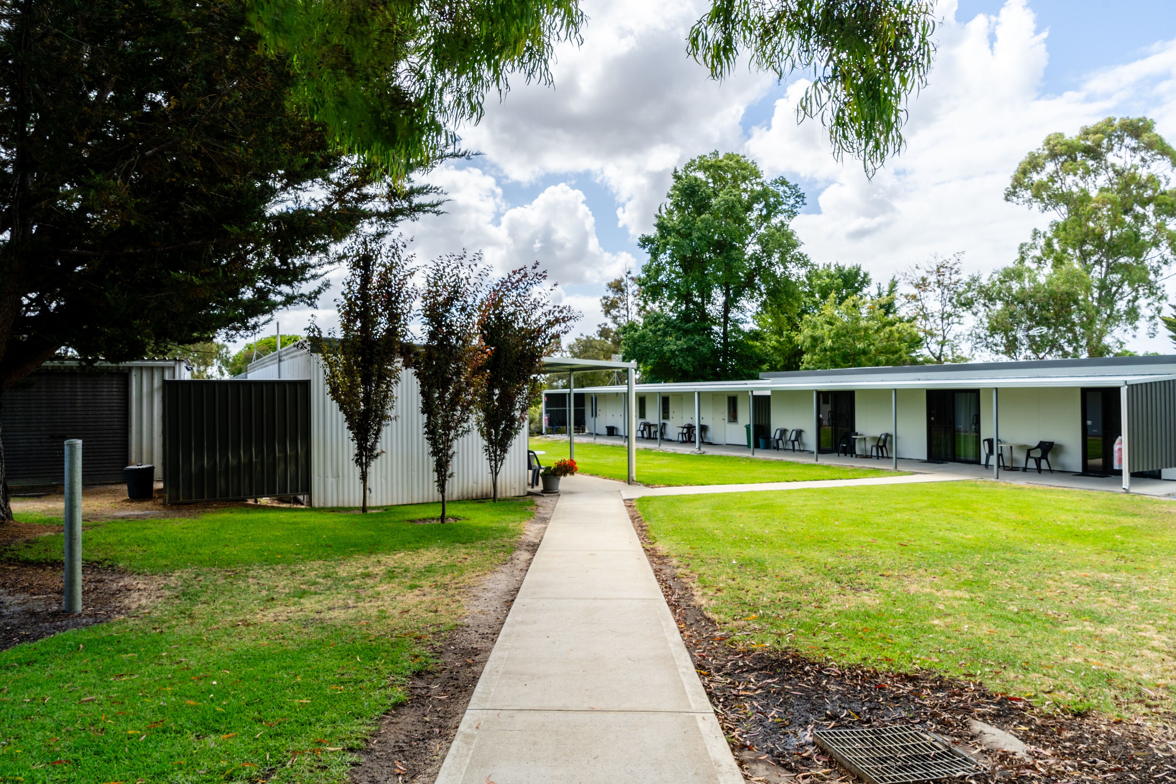 A pathway leading to a building with outdoor seating and a covered area.