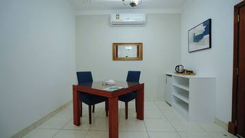 Una habitación con una mesa de comedor, sillas, un espejo, aire acondicionado y un estante con un hervidor.