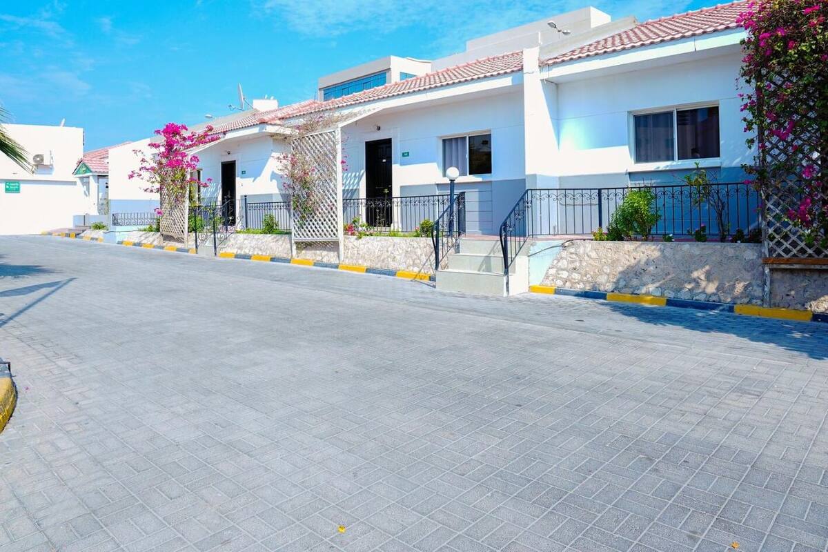 Une rue résidentielle bordée de maisons modernes, avec des trottoirs pavés et un ciel d’un bleu éclatant.