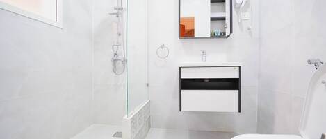 A modern bathroom with a glass-enclosed shower, a white sink with a mirror above it, and a toilet.