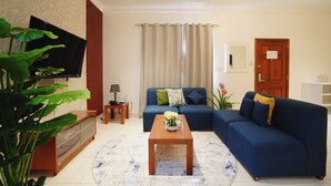 Una sala de estar con un sofá azul, una mesa de centro de madera, un televisor y una planta.