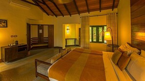A spacious bedroom with a large bed, wooden ceiling beams, a bedside table, and a window with curtains. - The Windflower Jungle Resorts and Spa (Gundlupet)