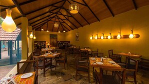 A restaurant with wooden tables and chairs, a tiled floor, and hanging light fixtures. - The Windflower Jungle Resorts and Spa (Gundlupet)