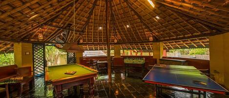 A room with a high ceiling, a pool table, a ping pong table, and a billiards table.
