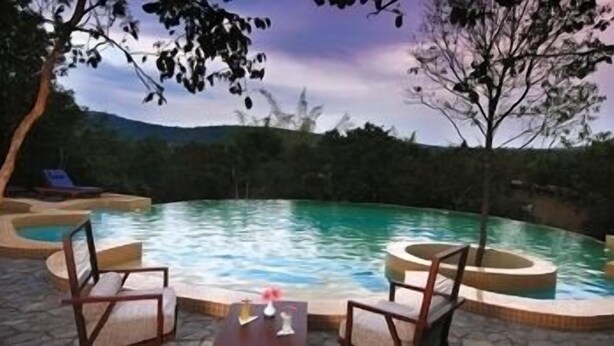 A circular pool with two lounge chairs and a small table, surrounded by trees and a mountainous backdrop. - The Windflower Jungle Resorts and Spa (Gundlupet)