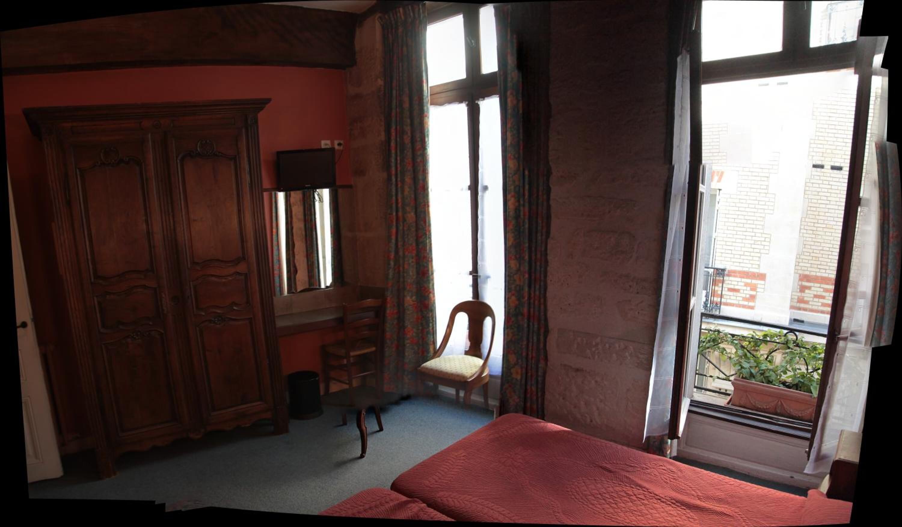 Une chambre dotée d’une grande armoire, d’une chaise, d’un lit et d’une fenêtre donnant sur des immeubles.