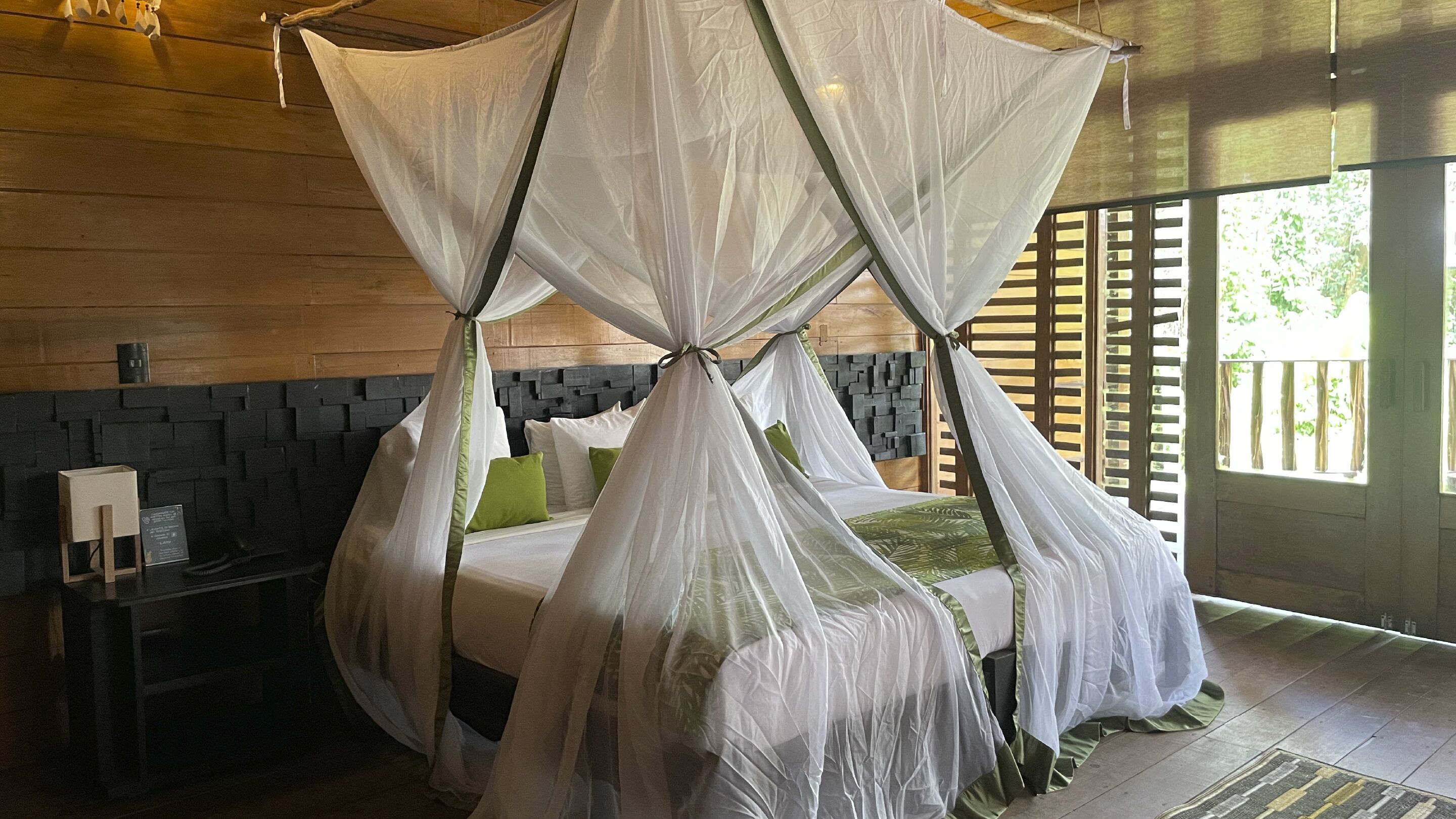 Une chambre avec un lit sous un dais, une table de chevet et une vue sur la verdure.