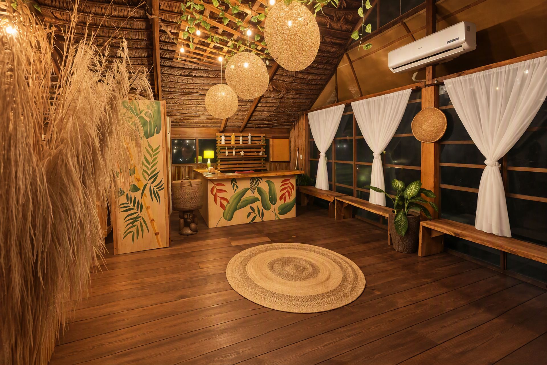 A room with a wooden floor, a round woven rug, a bench, a hanging light fixture, and a window with curtains.
