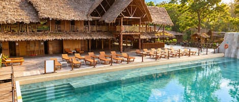 A poolside area with wooden lounge chairs and a thatched-roof building.