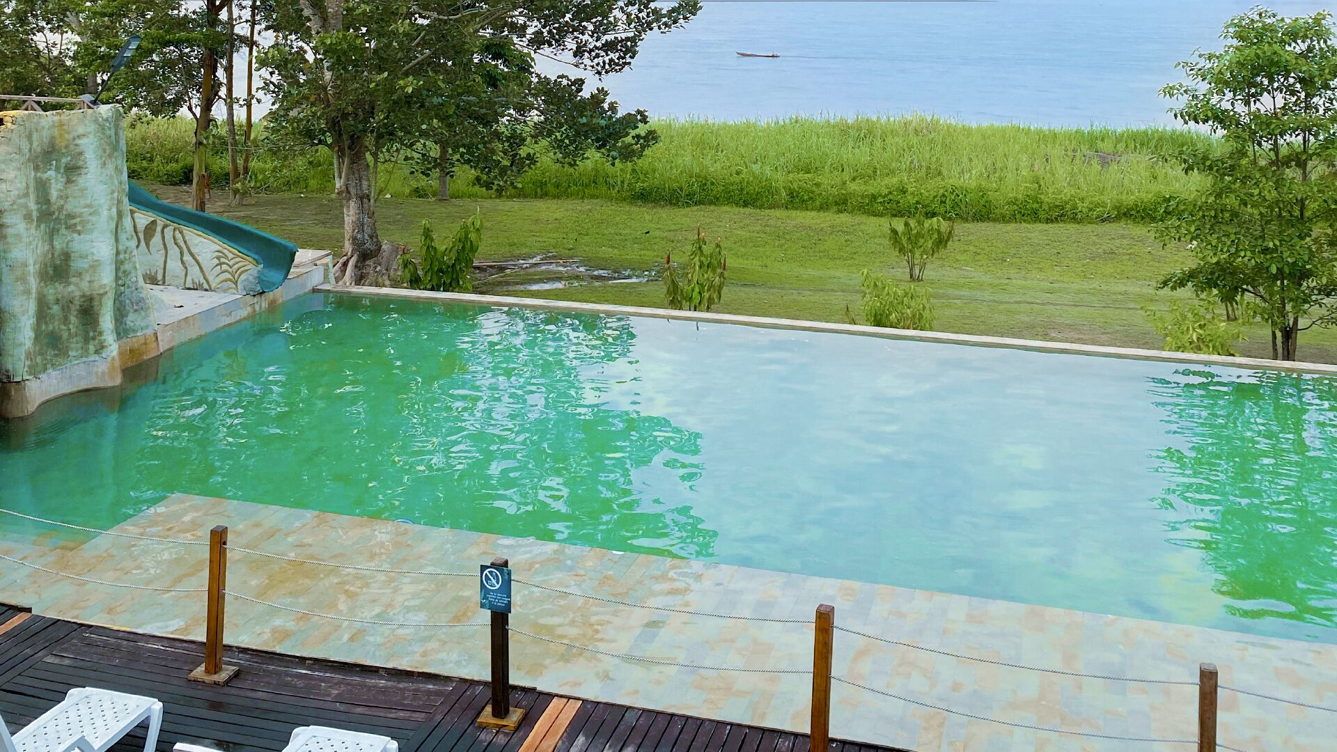 Piscina con tobogán, rodeada de vegetación y vistas al agua.