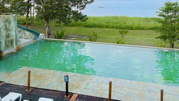 Piscina con tobogán, rodeada de vegetación y vistas al agua.