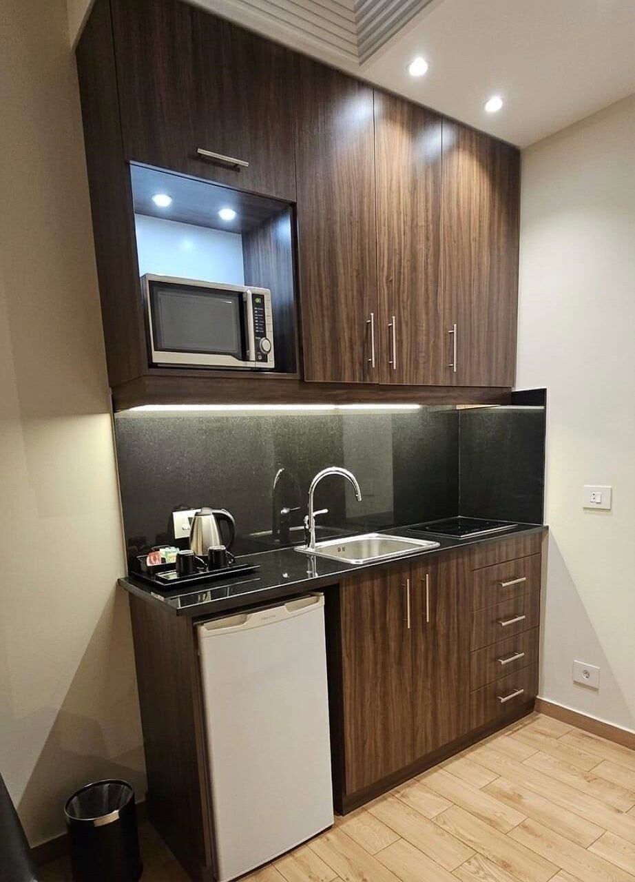 Cozinha compacta com armários de madeira escura, micro-ondas embutido, pia de aço inoxidável e máquina de lavar louça.