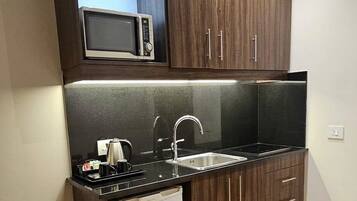 Cozinha compacta com armários de madeira escura, micro-ondas embutido, pia de aço inoxidável e máquina de lavar louça.