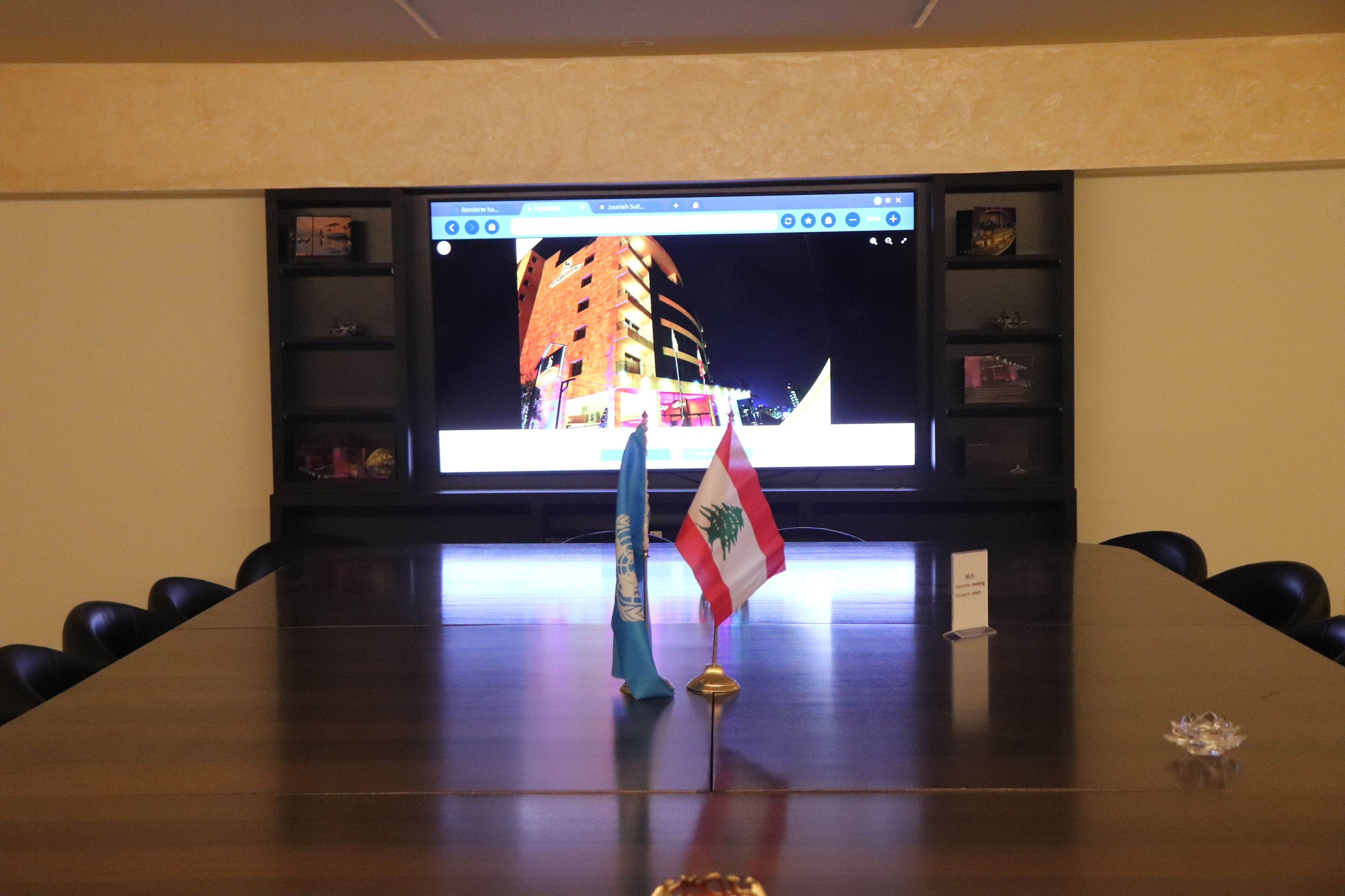 Un salón de conferencias con una televisión de pantalla plana grande mostrando un paisaje urbano, una bandera y una placa de identificación sobre la mesa.