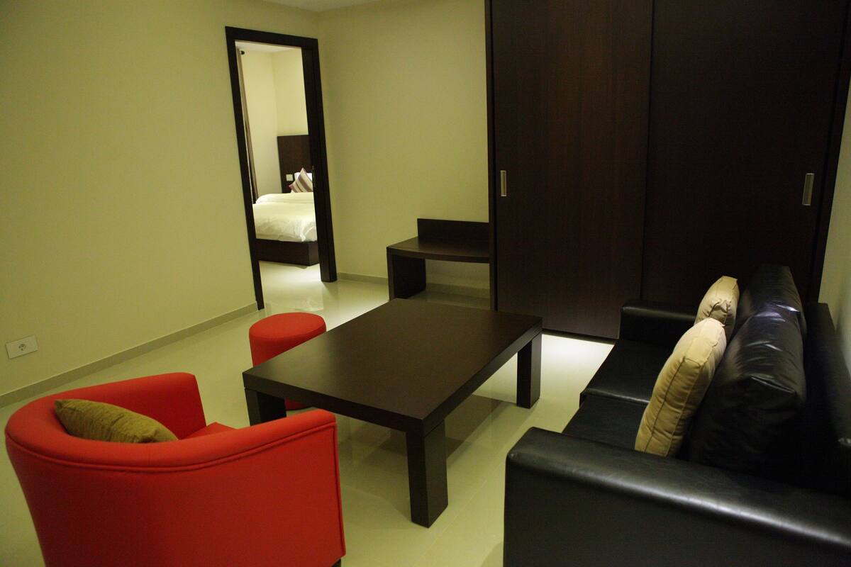 Un salon moderne avec un canapé foncé, un fauteuil rouge, une table basse noire et une petite table.