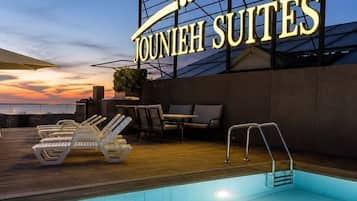 A hotel sign with 'Jounieh Suites' and a pool area with lounge chairs and a pool.