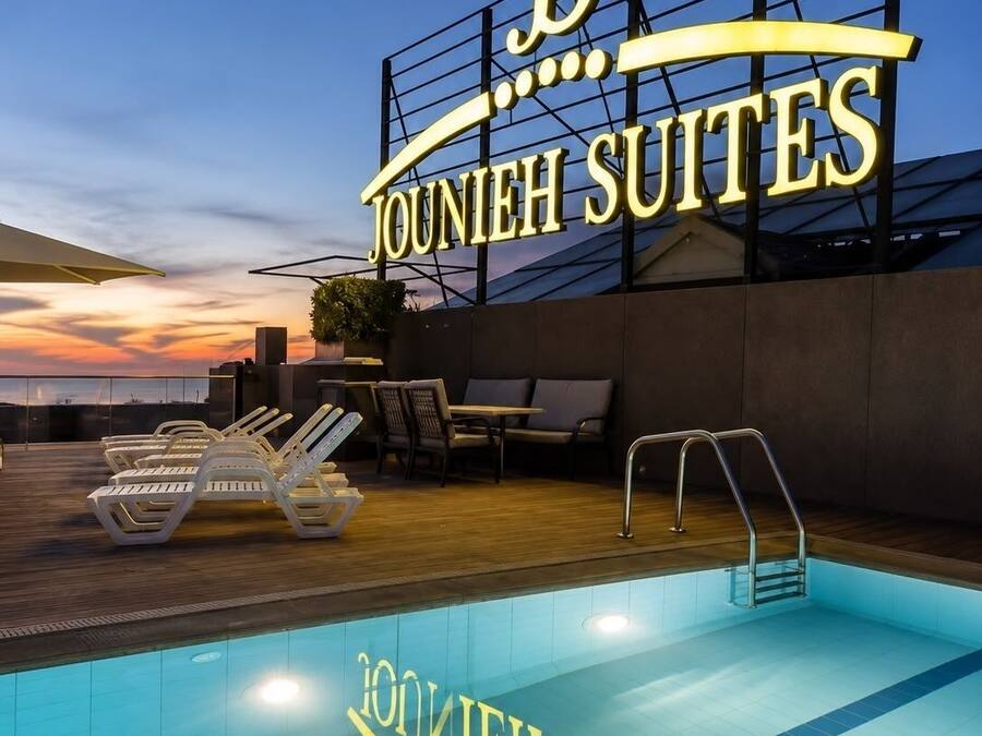 A hotel sign with 'Jounieh Suites' and a pool area with lounge chairs and a pool.