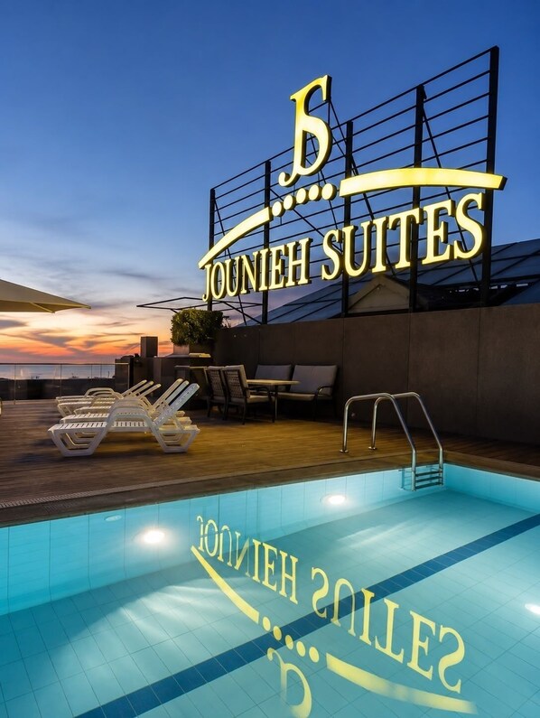 Señal de hotel que dice 'Jounieh Suites' y un área de piscina con sillones de descanso y una piscina.
