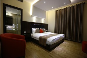 Habitación de hotel moderna con una cama grande, cabina de ducha de cristal, una silla roja y suelo de madera.