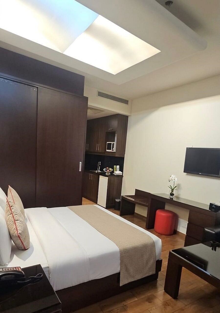 Una camera d'albergo con un letto, una scrivania, una TV, angolo cottura e un pouf rosso.